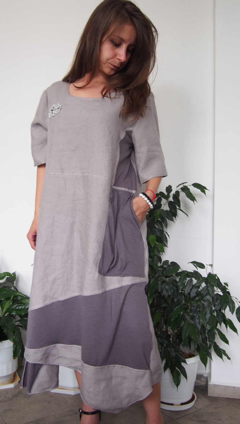 May include: A gray linen dress with a purple and gray patchwork design. The dress has a scoop neck, short sleeves, and a loose fit. It features a patch pocket on the left side.