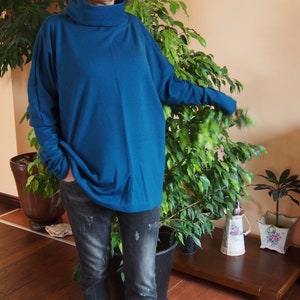 May include: A teal blue turtleneck sweater with long sleeves and a relaxed fit. The sweater is worn with dark wash jeans.