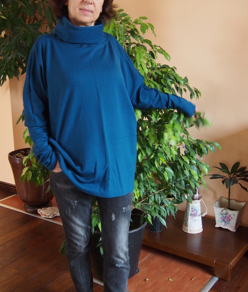 May include: A teal blue turtleneck sweater with long sleeves and a relaxed fit. The sweater is worn with dark wash jeans.