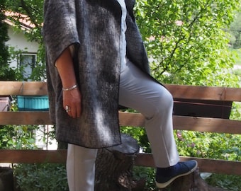 Può includere: Una donna indossa una giacca a maniche lunghe grigia e nera con un colletto nero e un paio di pantaloni grigi. È in piedi su un ceppo d'albero e indossa scarpe nere.
