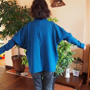 May include: A woman wearing a teal blue long-sleeved shirt with a relaxed fit and dark blue jeans.