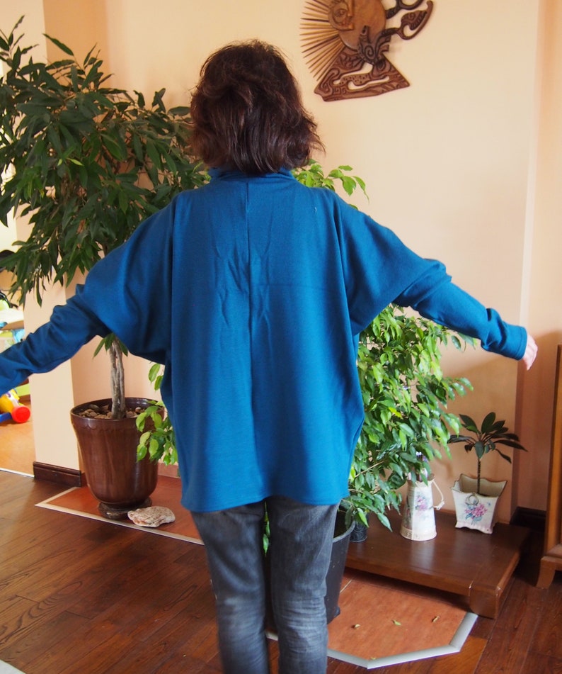 May include: A woman wearing a teal blue long-sleeved shirt with a relaxed fit and dark blue jeans.
