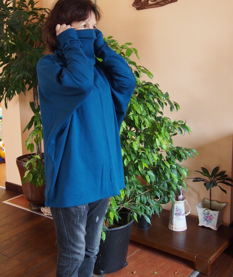 May include: A woman wearing a teal blue turtleneck sweater with long sleeves. The sweater is loose fitting and has a relaxed, casual style.