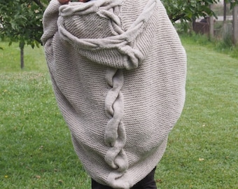Könnte beinhalten: Ein beigefarbener Strickcardigan mit einer großen Kapuze und einem geflochtenen Muster auf dem Rücken.