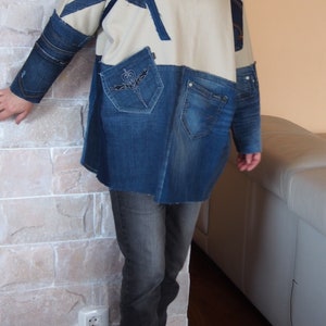 Peut inclure: Une veste en jean à manches longues avec un panneau blanc et des accents en jean. La veste a un col et une poche avec un motif brodé. La veste est portée sur une chemise rouge et associée à un jean gris foncé.