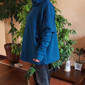 May include: A teal blue oversized sweater with a high neck and long sleeves. The sweater is made of a soft, comfortable fabric and has a relaxed fit.