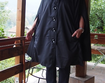 May include: A black hooded cape with a button fastening and pockets. The cape is made of a smooth, shiny fabric.