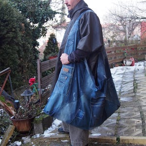 May include: A large, patchwork denim tote bag with multiple pockets and a blue button closure. The bag is made from recycled blue jeans and has a unique, handcrafted appearance. The bag is being carried over the shoulder.