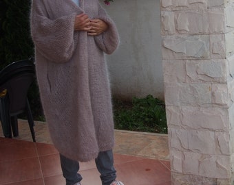 May include: A long, light pink cardigan with a loose fit and long sleeves. The cardigan is made of a soft, fuzzy material and has a V-neck.