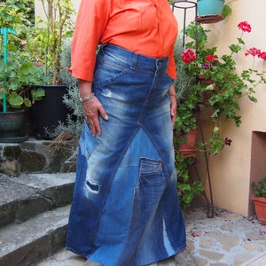 May include: A long denim skirt made from multiple panels of blue denim. The skirt has a high waist and a flowing silhouette. The skirt has several distressed areas and patches.