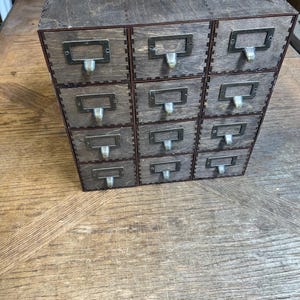 May include: A wooden drawer organizer with 12 small drawers. The drawers have metal pulls and are arranged in a 3x4 grid.