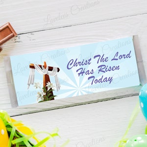 May include: A blue and white Easter chocolate bar wrapper with a cross and lilies. The text on the wrapper reads "Christ The Lord Has Risen Today".