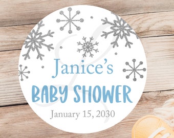 May include: A white circle with a blue and silver snowflake design. The text "Janice's Baby Shower" and "January 15, 2030" is printed on the circle.