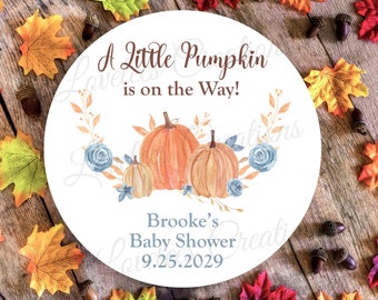 May include: A white round sticker with a watercolor illustration of pumpkins and blue flowers. The text reads "A Little Pumpkin is on the Way!" and "Brooke's Baby Shower 9.25.2029".