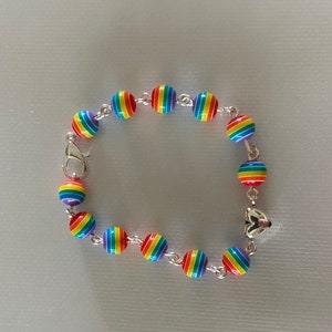 May include: A rainbow-striped bead bracelet with a silver clasp and connecting chain. The beads are round and feature a vibrant spectrum of colors. The bracelet is designed with a heart-shaped charm.