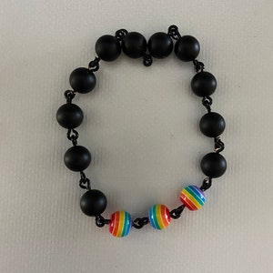 May include: A black beaded bracelet with rainbow-colored beads. The bracelet features matte black round beads strung together with a black chain. The rainbow beads have red, orange, yellow, green, blue, and purple stripes.