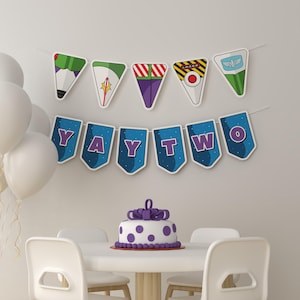 Puede incluir: Una escena festiva de cumpleaños con una pancarta que dice "YAY TWO" y banderines temáticos de personajes. Un pastel blanco con lunares morados y un lazo está sobre una mesa redonda. Globos blancos atados a un lado.