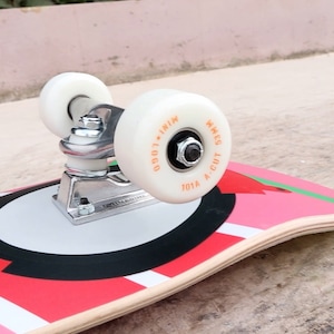 May include: A red, white, and black skateboard with a white wheel and a silver truck. The wheel has the text "101A A-CUT WHEELS LOGO - IN1N" printed on it.