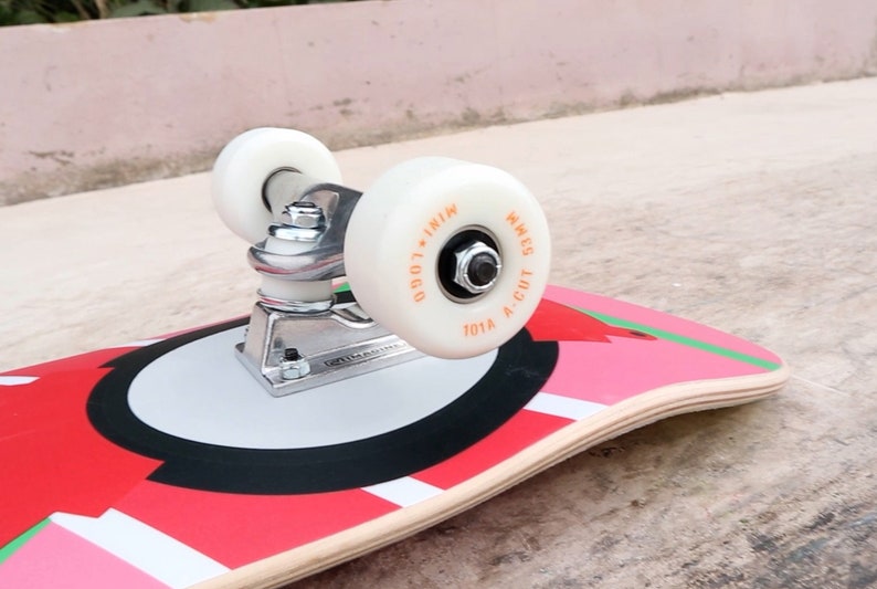 May include: A red, white, and black skateboard with a white wheel and a silver truck. The wheel has the text "101A A-CUT WHEELS LOGO - IN1N" printed on it.