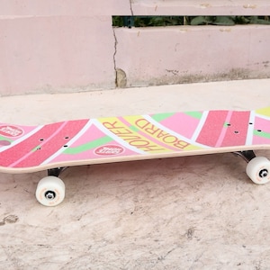 May include: A pink, yellow, and green skateboard with the words "Board Holler" printed on the deck.