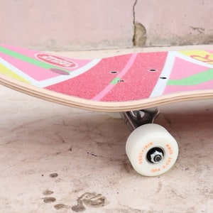 May include: A pink, green, and yellow skateboard with a white wheel. The skateboard has a graphic of a watermelon slice with the word "Fruit" on it.