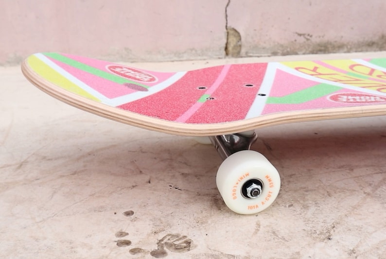 May include: A pink, green, and yellow skateboard with a white wheel. The skateboard has a graphic of a watermelon slice with the word "Fruit" on it.