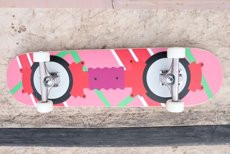 May include: A pink and red skateboard with black and white wheels. The deck has a geometric design with green accents.