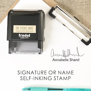 Puede incluir: Un sello autoentintable negro con el texto "THE PRINT MINT" y "theprintmint.etsy.com". El sello está junto a una pinza plateada, una firma y un bolígrafo turquesa. También se ve el texto "SIGNATURE OR NAME SELF-INKING STAMP".