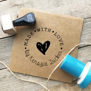 May include: A brown paper envelope stamped with a black heart and the words "MADE WITH LOVE by Kenszie Zucker" in a circular design. A black stamp and a blue stamp are visible.