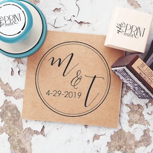 May include: A selection of stamps and a kraft paper card with a circular design. The card displays the initials "M & T" and the date "4-29-2019" in black script. The stamps include the text "the PRINT mint" in a script font.