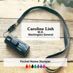 May include: A black pocket name stamper with a black lanyard. The text "Caroline Linh M.D. Washington General" is printed on a white rectangle. Below the text is the phrase "Pocket Name Stamper" and a row of colourful ink drop icons.