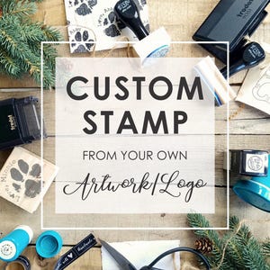 May include: An overhead shot of custom stamps and related supplies on a wooden surface. The image features stamps with paw prints and a cat design, along with the text "CUSTOM STAMP FROM YOUR OWN Artwork/Logo."
