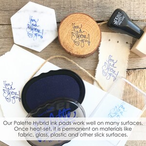 Peut inclure: Plusieurs objets estampill&eacute;s de l'expression "I'm glad you're here !" &agrave; l'encre bleue. On y trouve un dessous de verre en marbre, une tranche de bois et du tissu. Un tampon encreur bleu marine et un tampon sont &eacute;galement visibles.