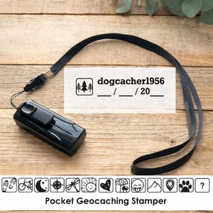 May include: Black pocket geocaching stamper with a black lanyard. The stamper has the text "dogcacher1956" and a series of icons. The stamper is on a wooden surface.