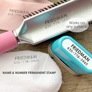 May include: A pink-handled hairbrush, a light blue stamp, and a white cloth are displayed. Each item is imprinted with the name "FRIEDMAN" and a phone number. The stamp has the text "NAME & NUMBER PERMANENT STAMP" and "Works on any surface!"