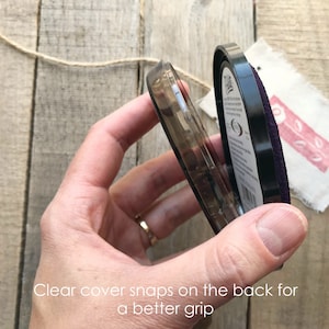 Peut inclure: Un tampon encreur noir avec un couvercle en plastique transparent. Le couvercle est ouvert, r&eacute;v&eacute;lant le tampon encreur violet. Le texte sur le tampon encreur indique "Clear cover snaps on the back for a better grip."