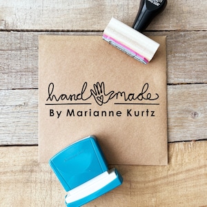 May include: A kraft paper card with the words "handmade By Marianne Kurtz" in black script and a hand-shaped graphic. A black and white stamp and a blue ink pad are also visible.
