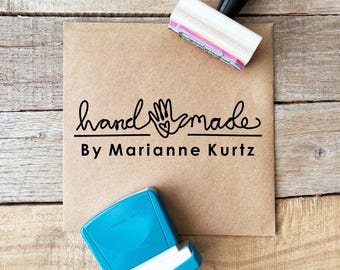May include: A kraft paper card with the words "handmade By Marianne Kurtz" in black script and a hand-shaped graphic. A black and white stamp and a blue ink pad are also visible.