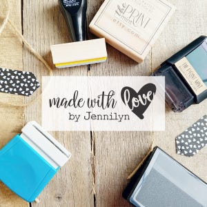 May include: An overhead shot of various stamps and accessories on a wooden surface. The text "made with love by Jennilyn" is prominently displayed. Other stamps include "the PRINT MINT .etsy.com" and heart-shaped tags.