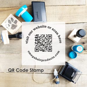 Puede incluir: Una colección de sellos y almohadillas de tinta sobre una superficie de madera. Incluye un sello de código QR con el texto "visit our website or scan here" y "omegahairproducts.com". Otros sellos incluyen una huella de pata y el texto "Love, Minnie".