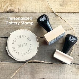 Può includere: Un timbro per ceramica personalizzato con il testo "Pottery by Matt Voletta" che circonda le iniziali "M/V". Due timbri con manici neri e blocchi di legno sono accanto all'argilla timbrata. Il testo "Personalized Pottery Stamp" è in alto a sinistra.