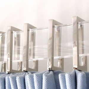 Row of silver rectangular curtain rings in shiny polished nickel finish.