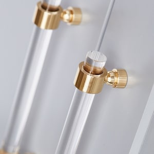 Set of clear lucite cabinet door handles or pulls with a crown post hardware base, finished in polished brass. The pair of pulls are installed on light grey cabinetry.