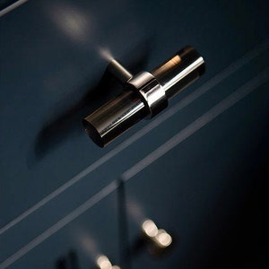 May include: A silver T-shaped cabinet pull with a polished finish. The pull is mounted on a dark blue cabinet door.
