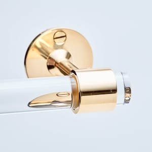 Detail shot of polished brass hardware ring fitted around a acrylic rod to be used as a wall mounted toilet paper holder.