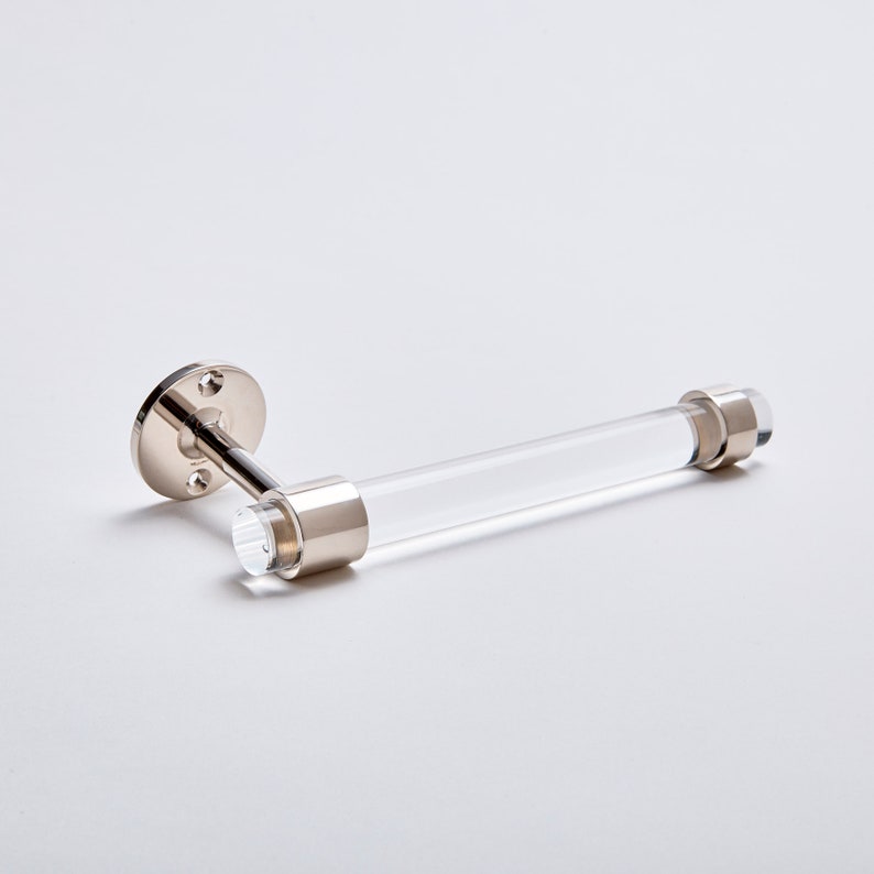 A clear lucite tubular rod fitted in two brass rings on both ends. One ring is attached to mounting hardware to install on a wall for the item to be used as a toilet paper holder. The hardware is solid brass, finished in polished nickel.