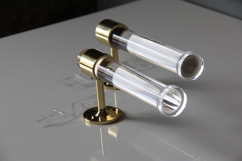 Two transparent glass tubes with brass bases are placed on a white surface, creating a minimalist and elegant design.