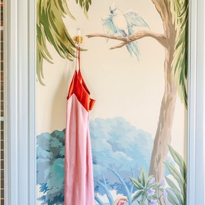 Tropical mural featuring Luxholdups angled lucite robe hook with brass hardware, wall mounted and holding a red and pink dress.