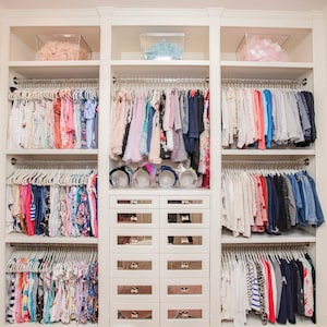Walk in closet featuring children's clothing hanging from lucite rods.