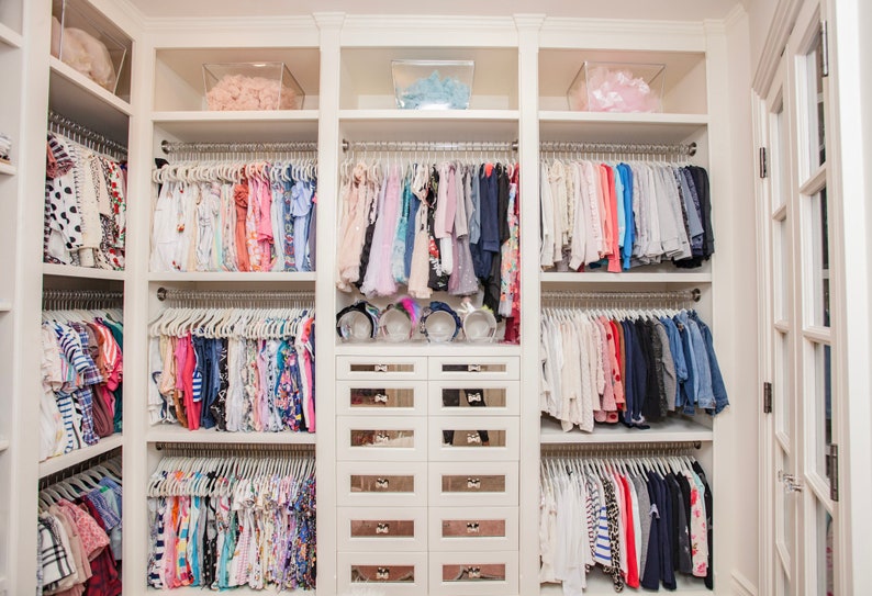 Walk in closet featuring children's clothing hanging from lucite rods.